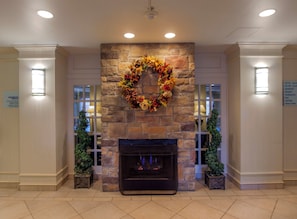 A stone fireplace with a decorative wreath, flanked by two potted plants. - Holiday Inn Express Hotel & Suites Buffalo-Airport by IHG (Buffalo)