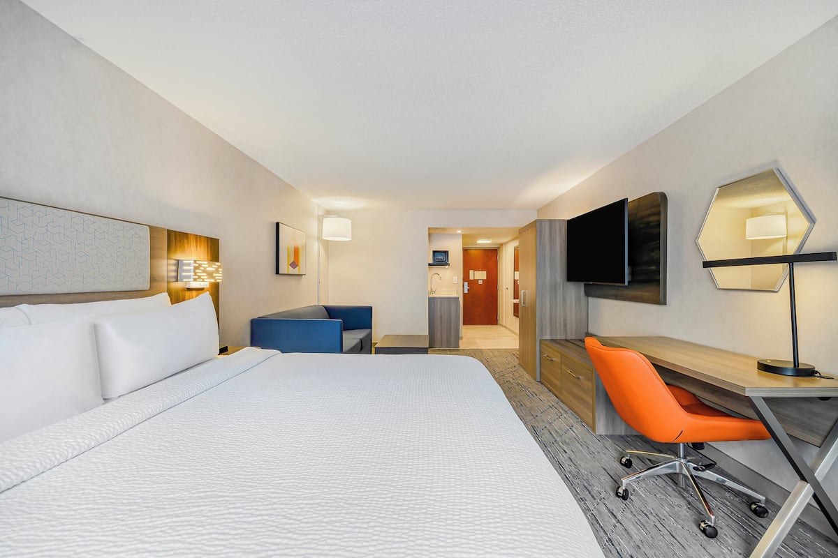 Ett hotellrum med en stor säng, ett skrivbord med en orange stol, en platt-TV och en väggmonterad lampa.