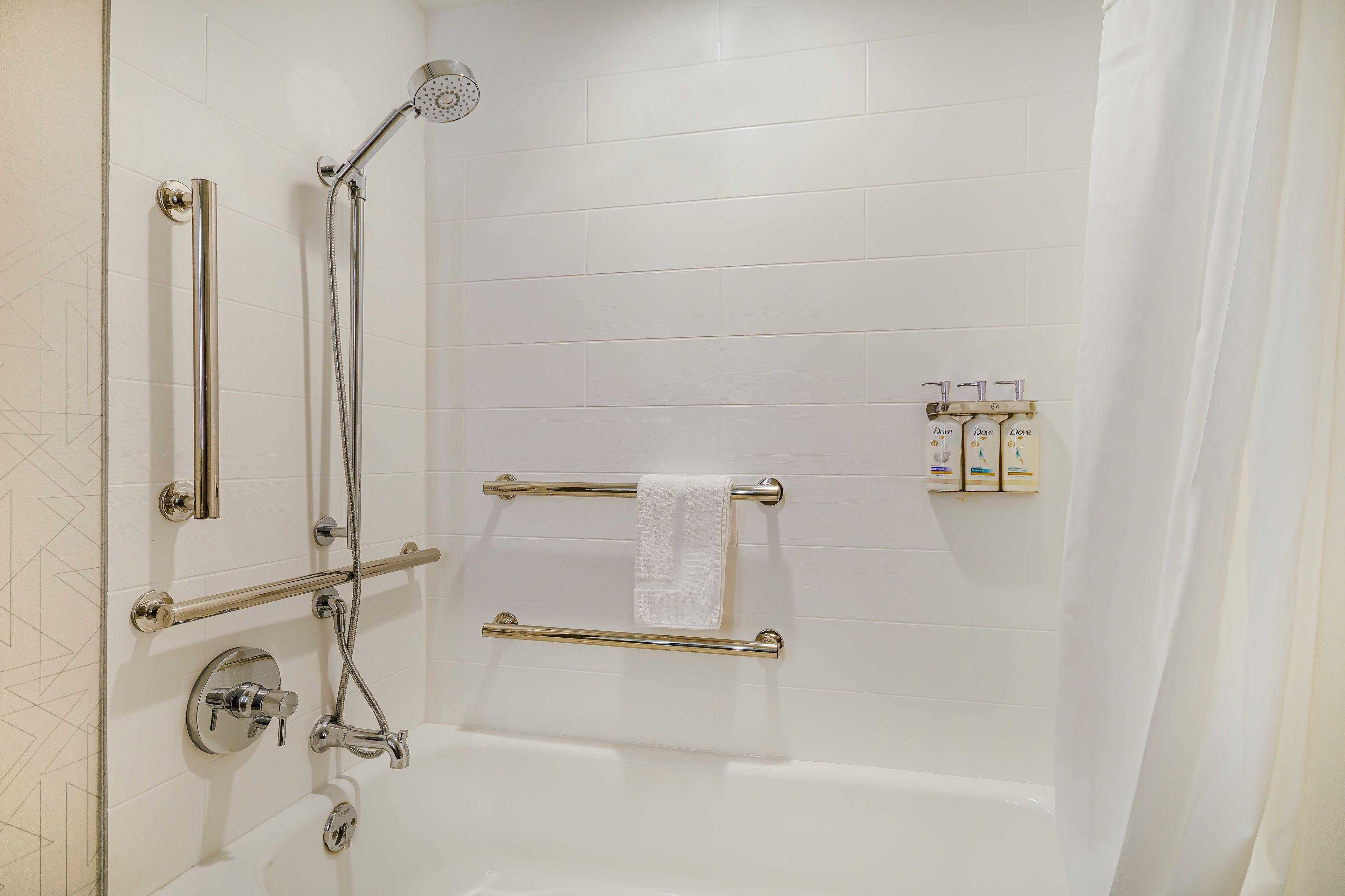 A modern bathroom with a walk-in shower, grab bars, a towel rack, and a soap dispenser.
