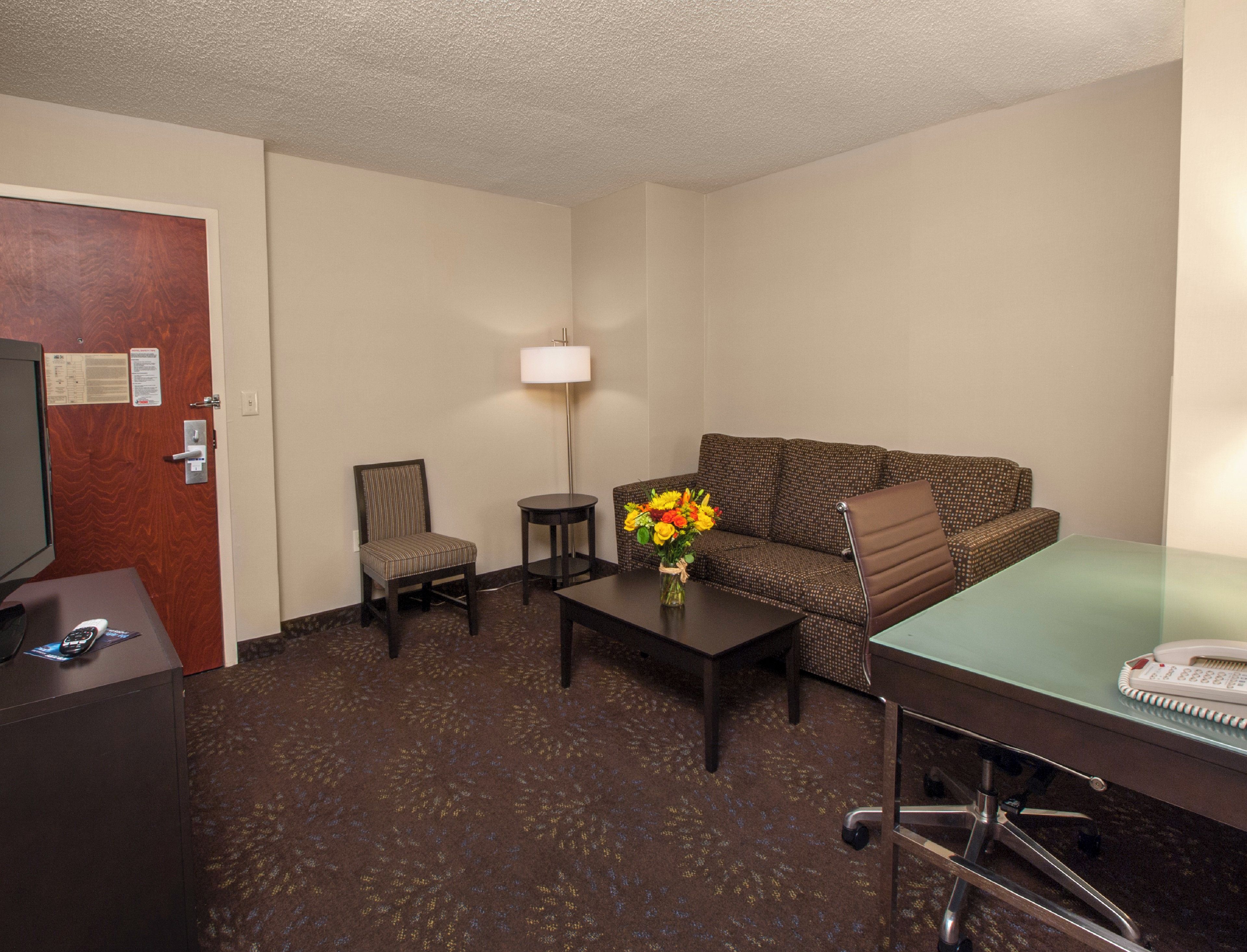 Een hotelkamer met een bank, fauteuil, een klein tafeltje, lamp en een bureau met telefoon.