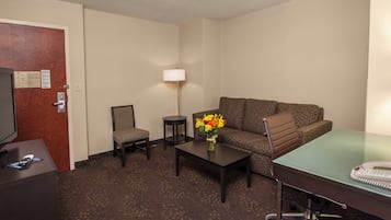 Een hotelkamer met een bank, fauteuil, een klein tafeltje, lamp en een bureau met telefoon.