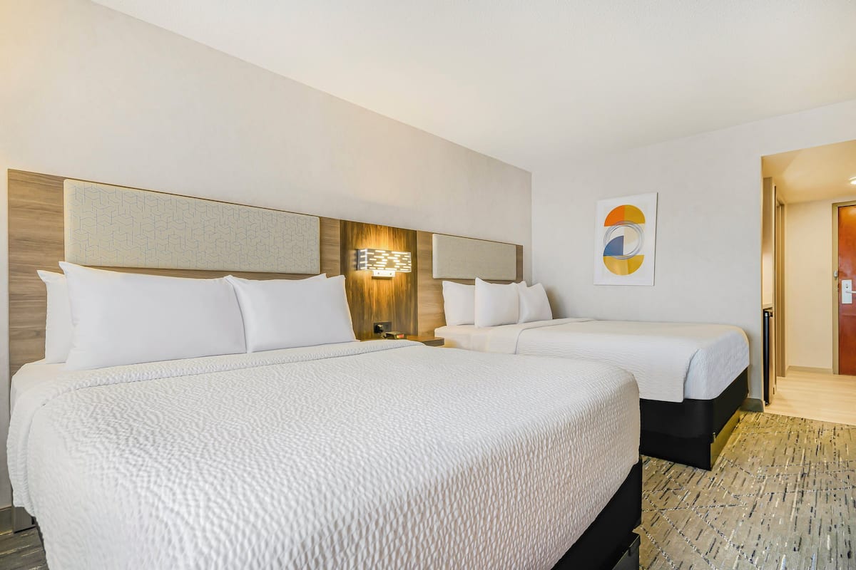 Ett hotellrum med två sängar, en sänggavel i trä, en vägglampa och ett inramat konstverk.