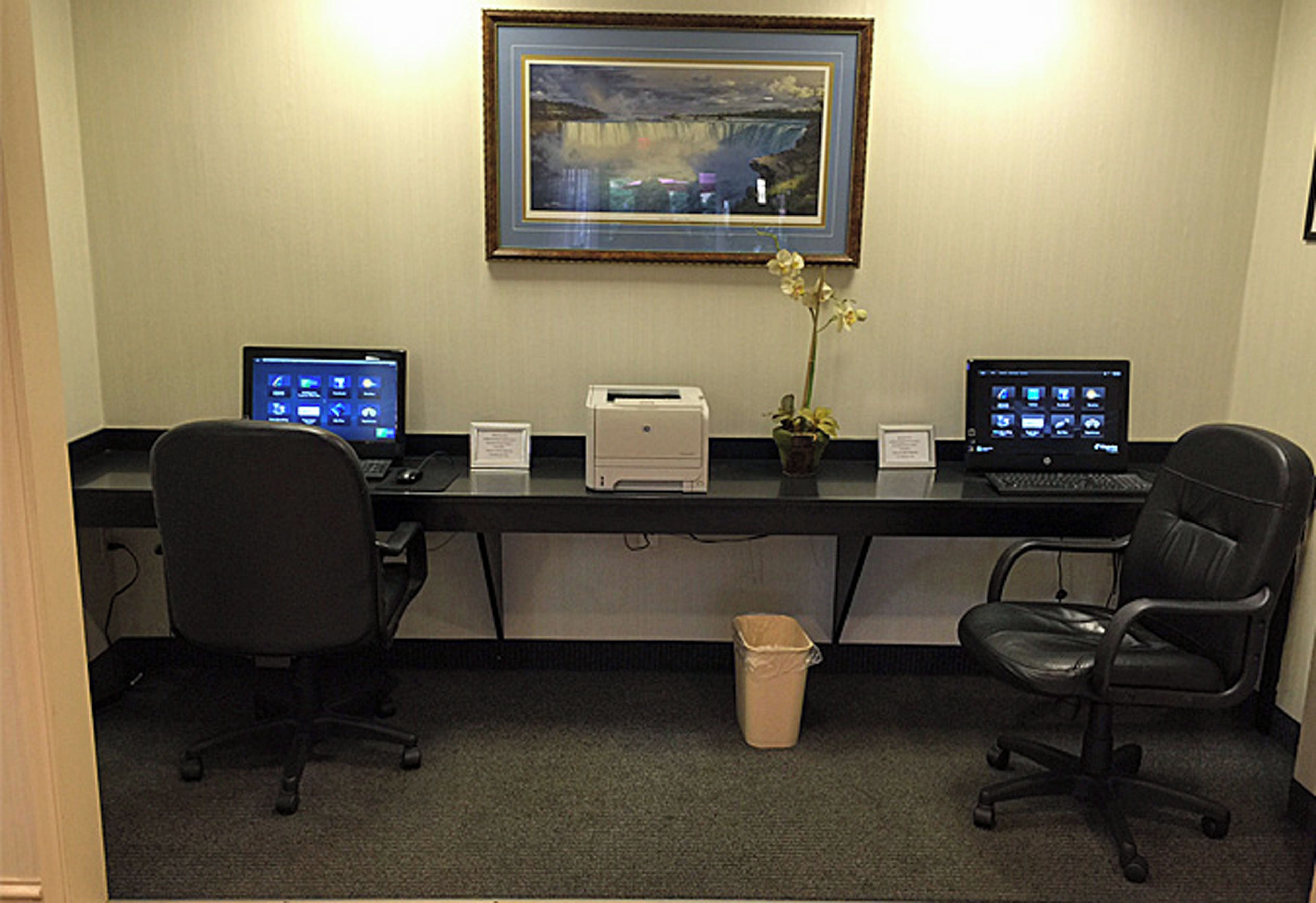 A workspace with two desks, computers, chairs, a printer, and a framed picture on the wall.