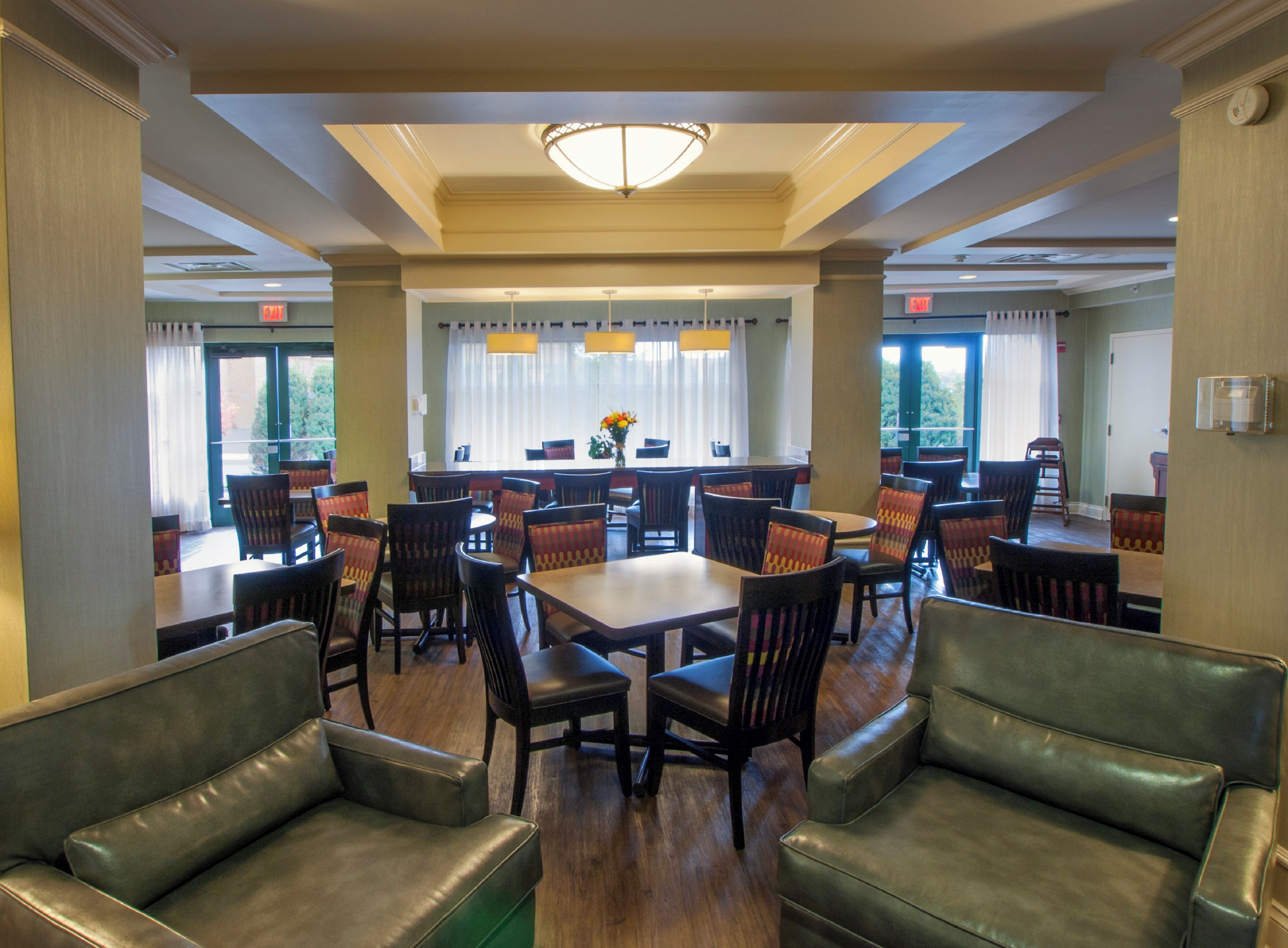 A dining area with tables and chairs, a chandelier, and windows with curtains.