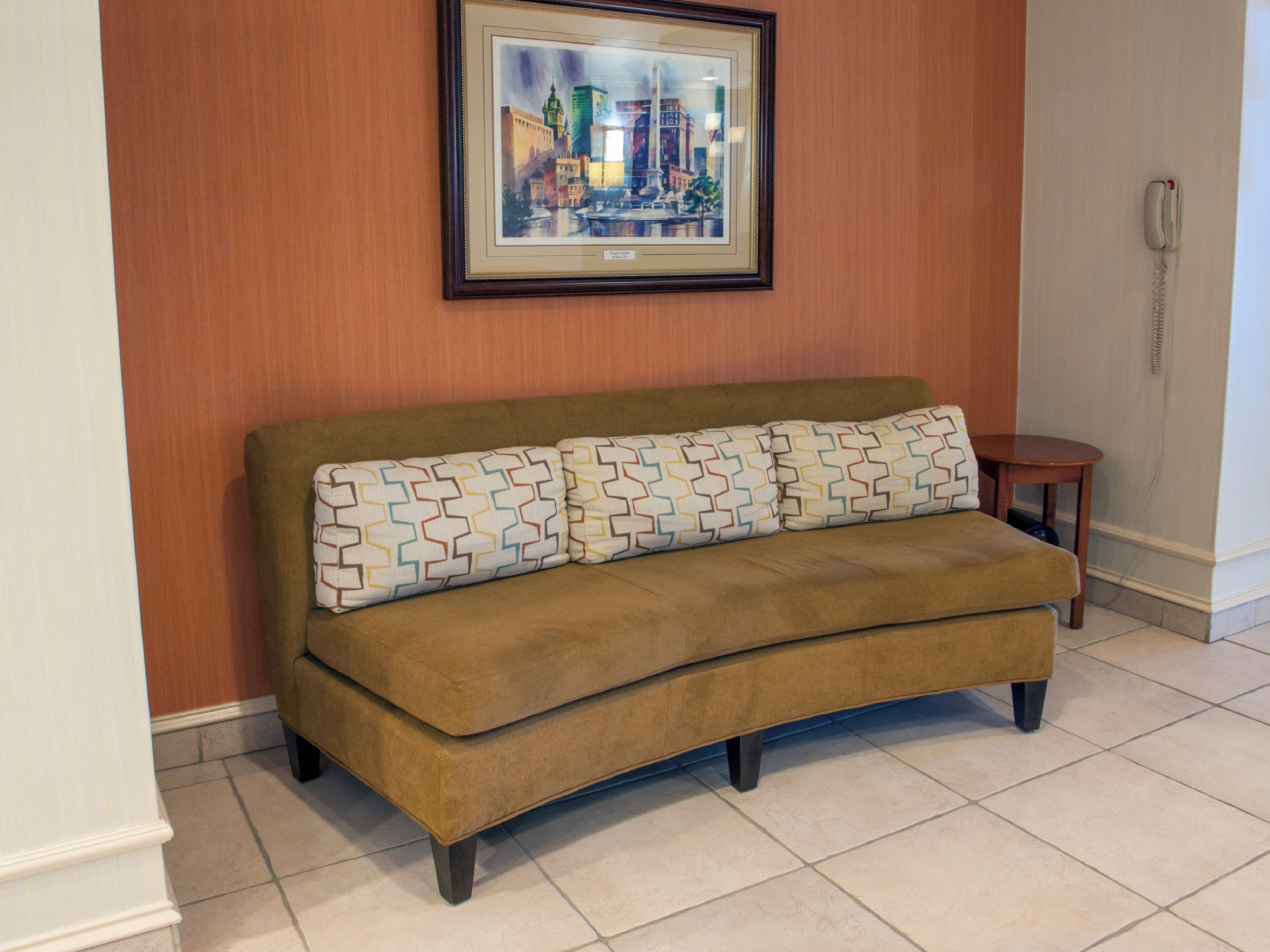 A brown sofa with patterned cushions against a wall with a framed cityscape painting.