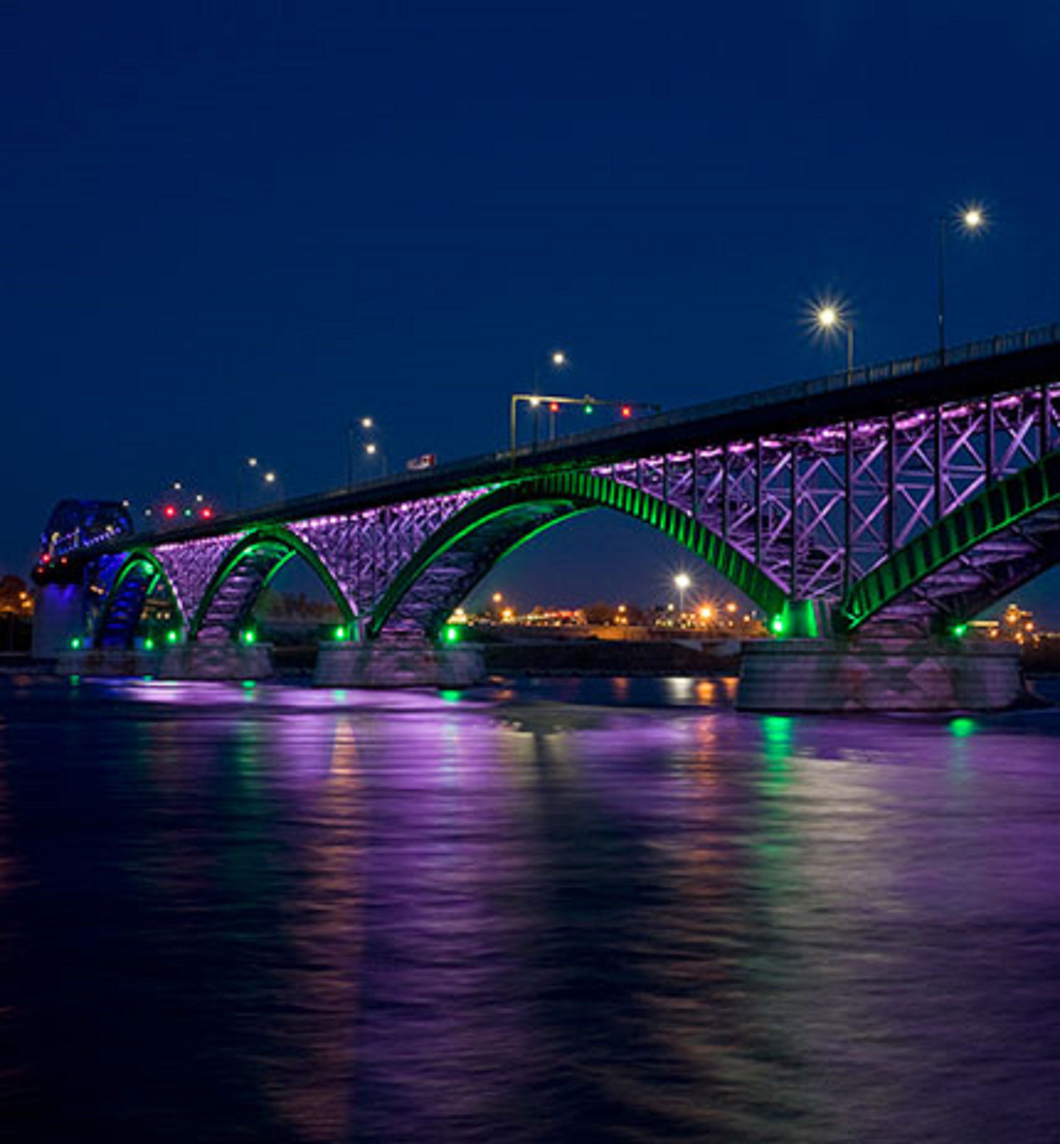 Un ponte con più archi illuminati da luci viola e verdi, che si estende su un corso d'acqua.