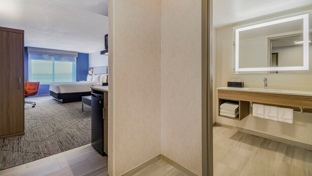 A hotel room with a bed, desk, and a large mirror with built-in lighting.