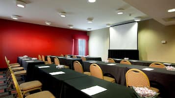 A conference room with multiple tables and chairs, a projector screen, and a red accent wall.