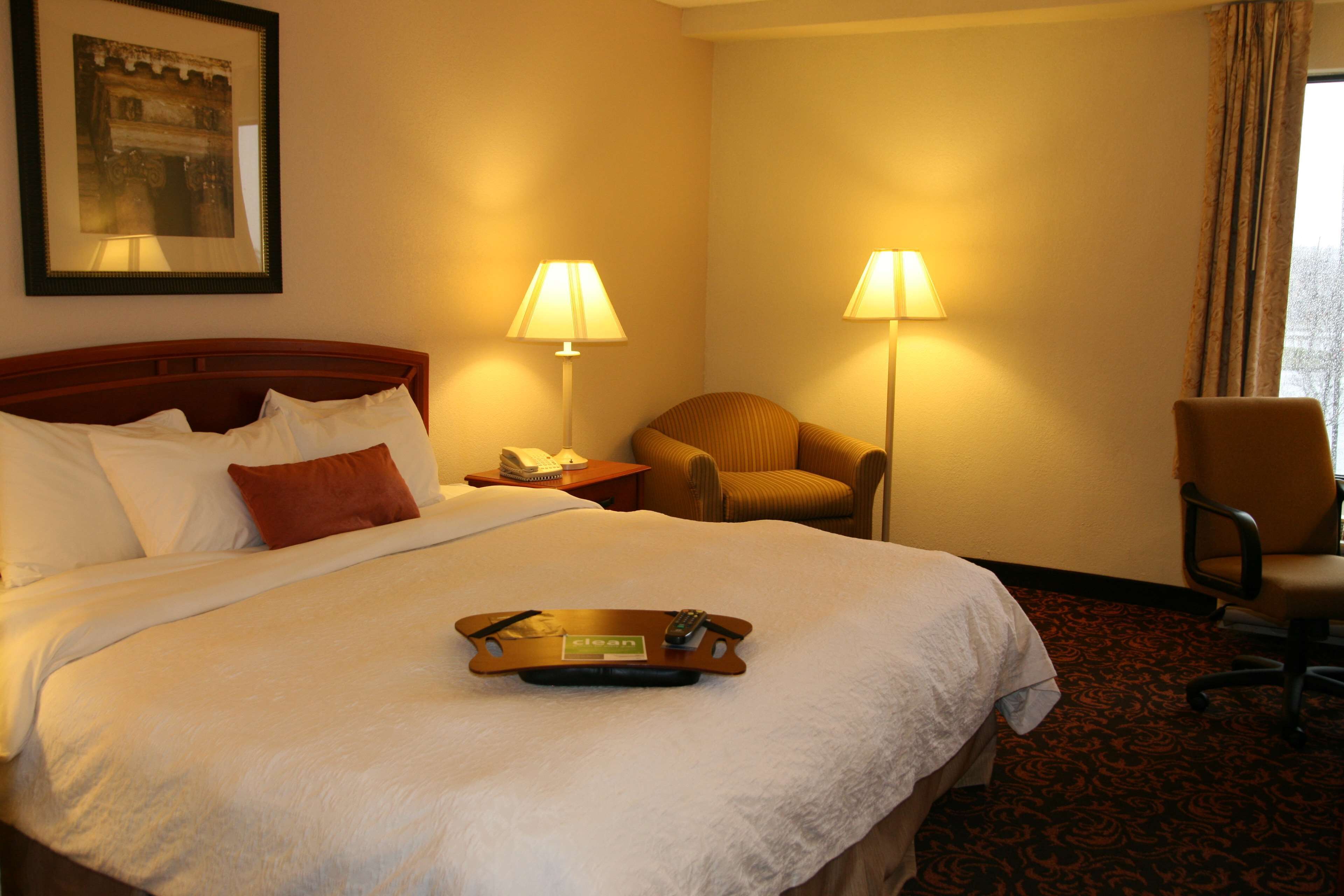 Una habitación de hotel con una cama grande, dos lámparas de noche, una silla, un escritorio y una bandeja con un control remoto.