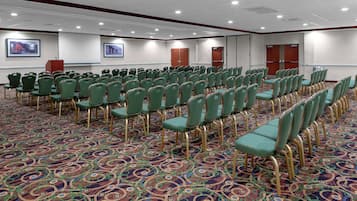 A conference room with rows of green chairs and a patterned carpet.