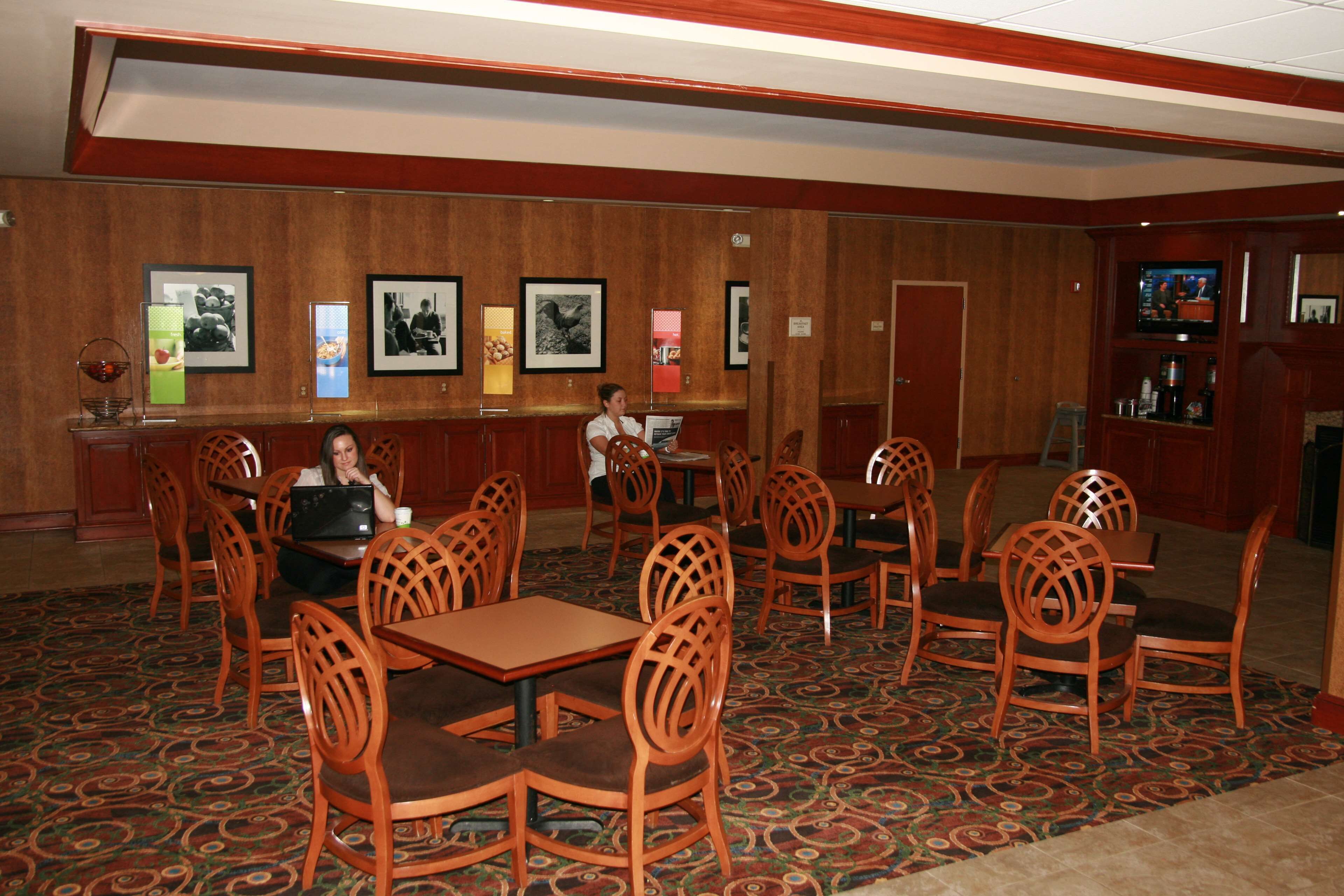 A restaurant with wooden chairs and tables, a bar area, and framed pictures on the walls.