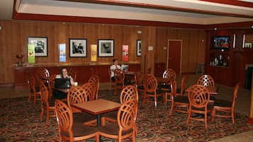 A restaurant with wooden chairs and tables, a bar area, and framed pictures on the walls.