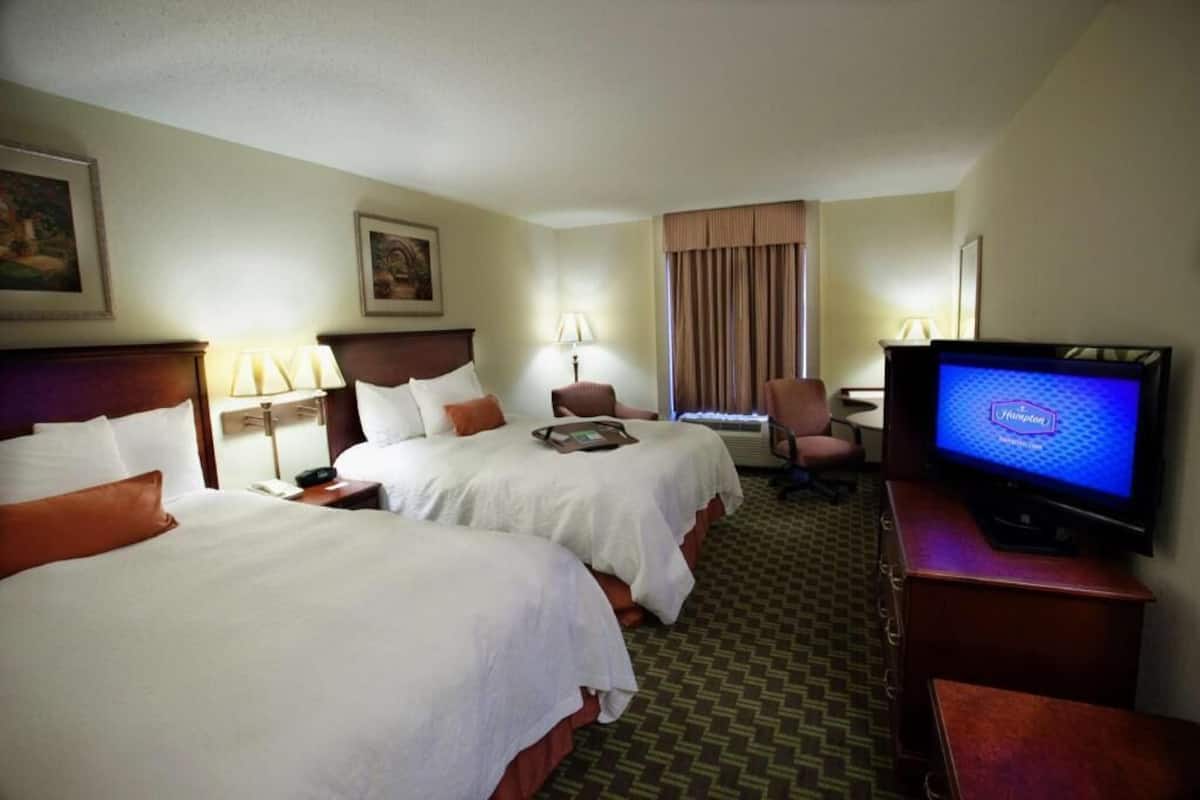 A hotel room with two beds, a desk with a television, and a chair.