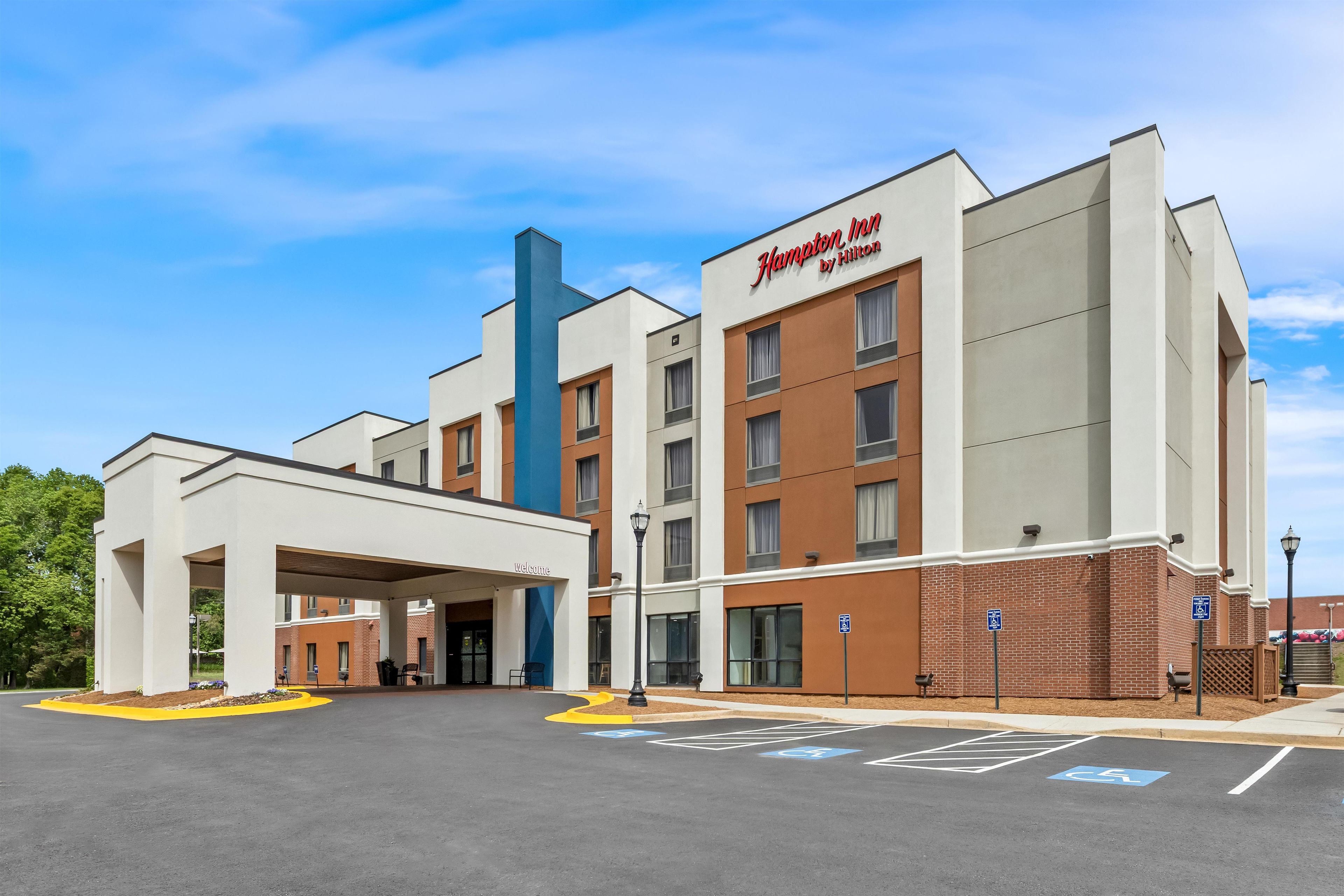 A Hampton Inn by Hilton hotel with a modern design, a covered entrance, and designated handicapped parking spaces.
