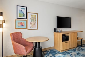 A hotel room with a single round table, a red upholstered chair, a flat-screen TV mounted on the wall, and a wooden cabinet with a microwave. - Hampton Inn Carrollton (Carrollton)