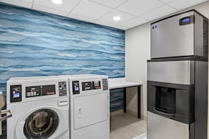 Una unidad de lavadora y secadora para uso comercial, con paneles de control, dispensador de agua y refrigerador de acero inoxidable.