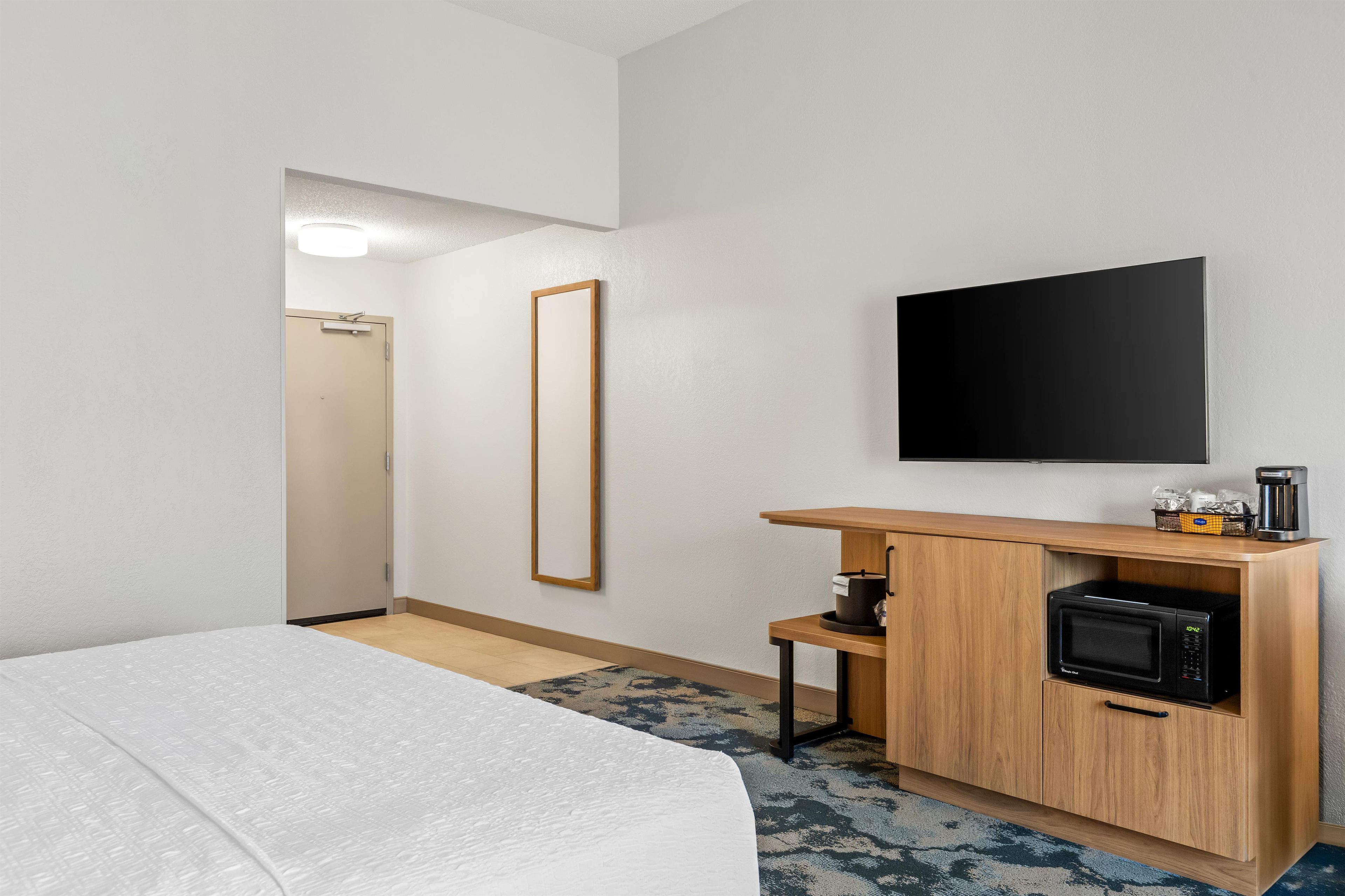 Quarto de hotel com cama, televisão, espelho, máquina de café e micro-ondas.
