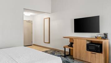Quarto de hotel com cama, televisão, espelho, máquina de café e micro-ondas.