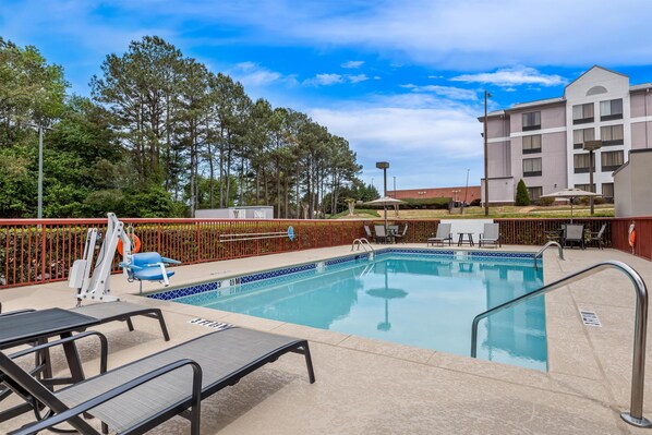 A swimming pool with lounge chairs, a lifeguard stand, and a fenced area.