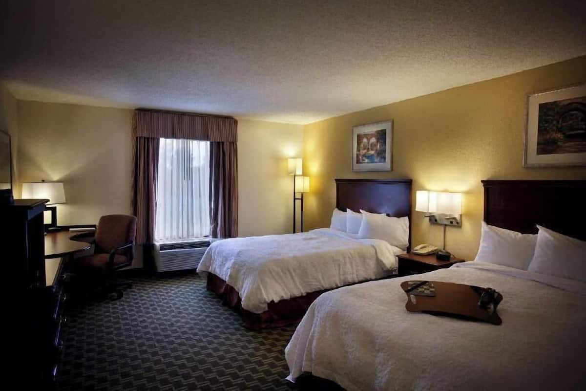 A hotel room with two beds, a desk, a chair, and a window with curtains.