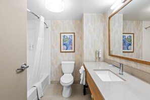 A modern bathroom with a bathtub, toilet, and sink. There are framed pictures on the wall and a large mirror above the sink.