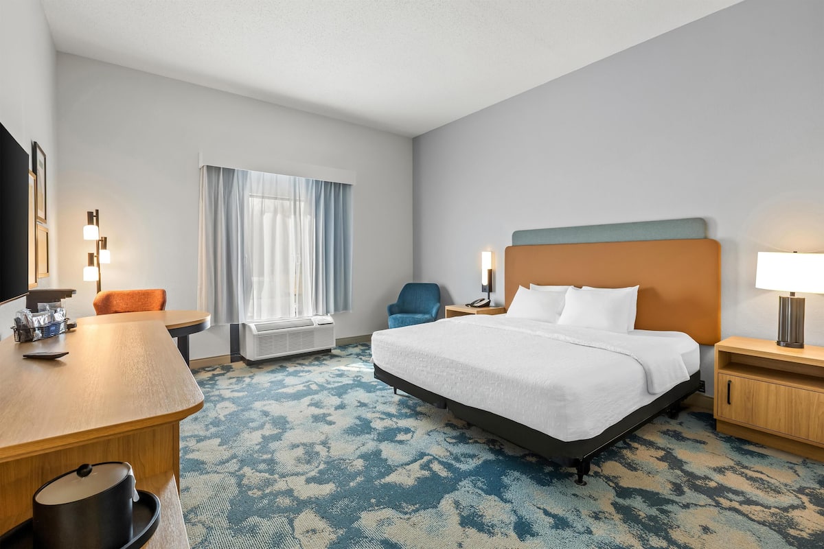 A hotel room with a bed, a desk, a chair, a lamp, and a window with curtains.