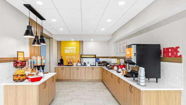 A modern kitchen area with a central counter, wooden cabinets, and a coffee station. - Hampton Inn Carrollton (Carrollton)
