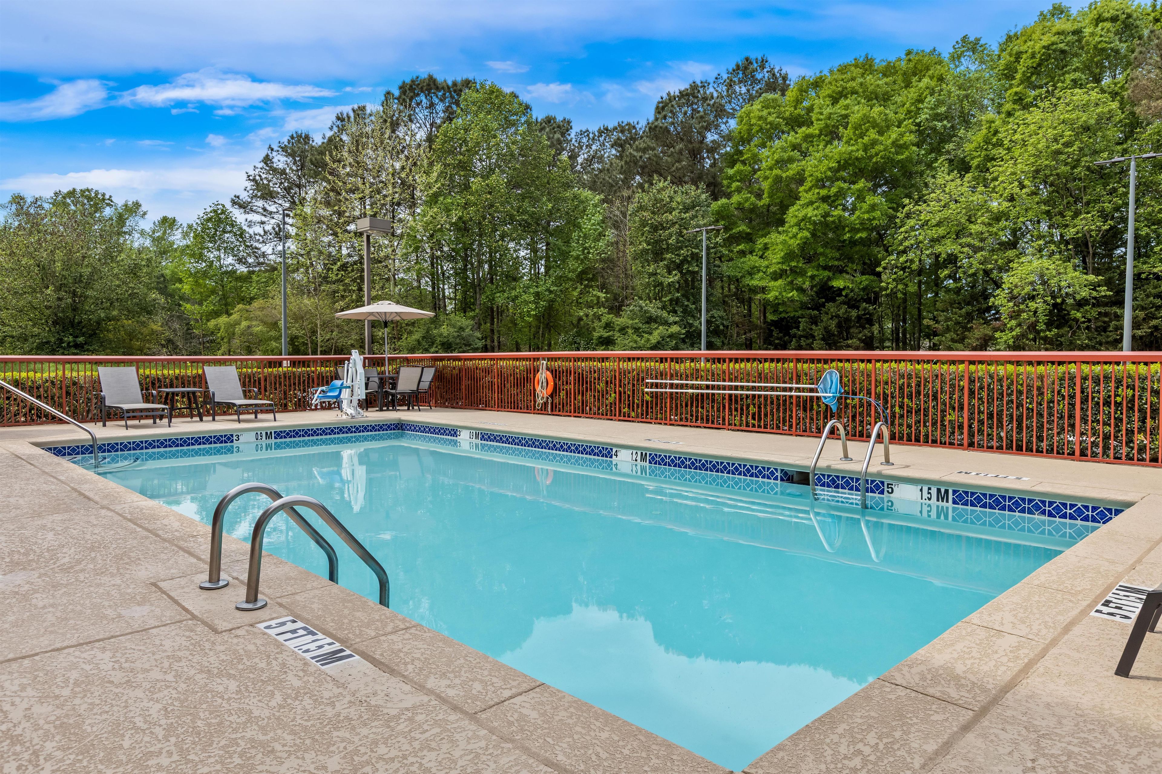 A rectangular swimming pool with a tiled edge, surrounded by a red fence, and equipped with a ladder.