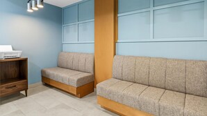 A room with a blue wall, a wooden column, two grey sofas, a wooden shelf with a laptop, and a ceiling light fixture. - Hampton Inn Carrollton (Carrollton)