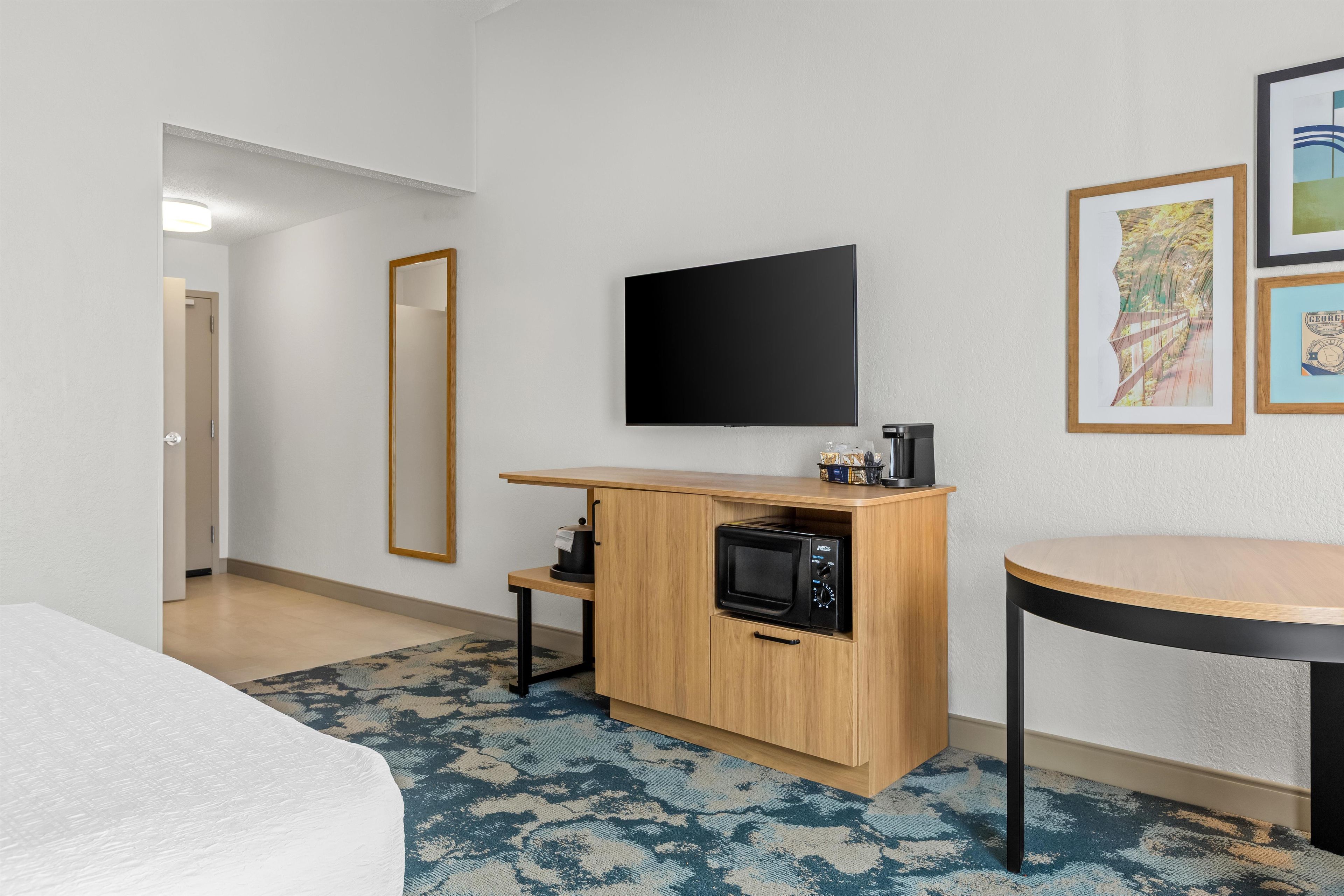 A hotel room with a bed, a small kitchenette with a microwave, a flat-screen TV, and a round table.