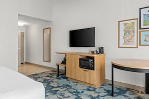 Una habitación de hotel con una cama, una kitchenette pequeña con microondas, un televisor de pantalla plana y una mesa redonda.