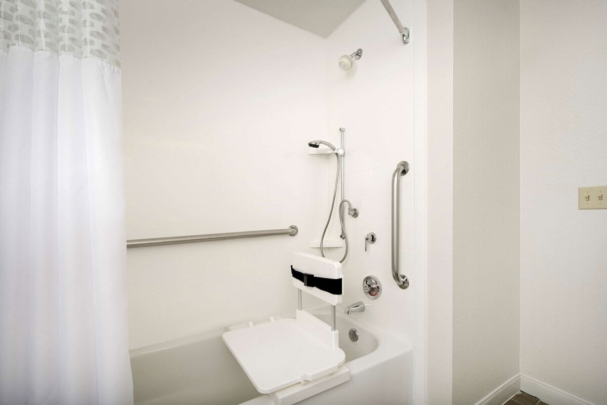 Une salle de bain équipée d’une douche, de barres d’appui, d’un lavabo blanc et de toilettes.