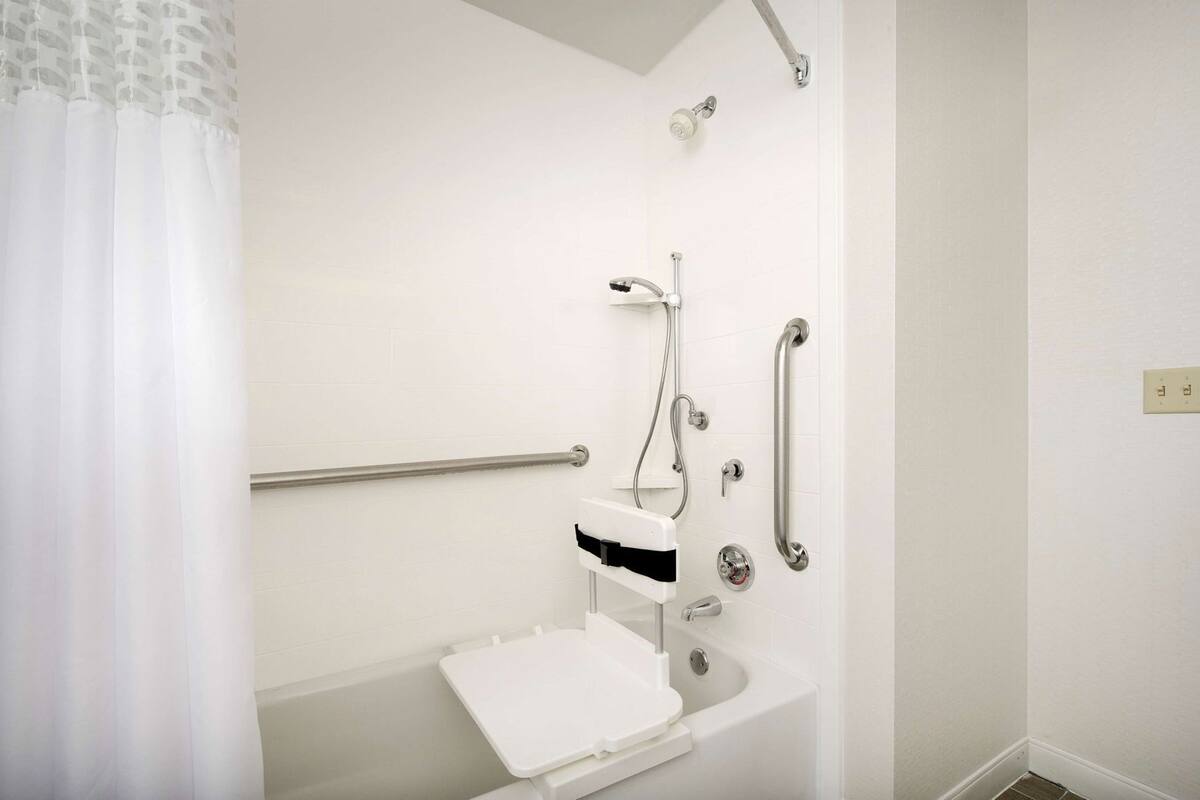 A bathroom with a shower, grab bars, a white sink, and a toilet.