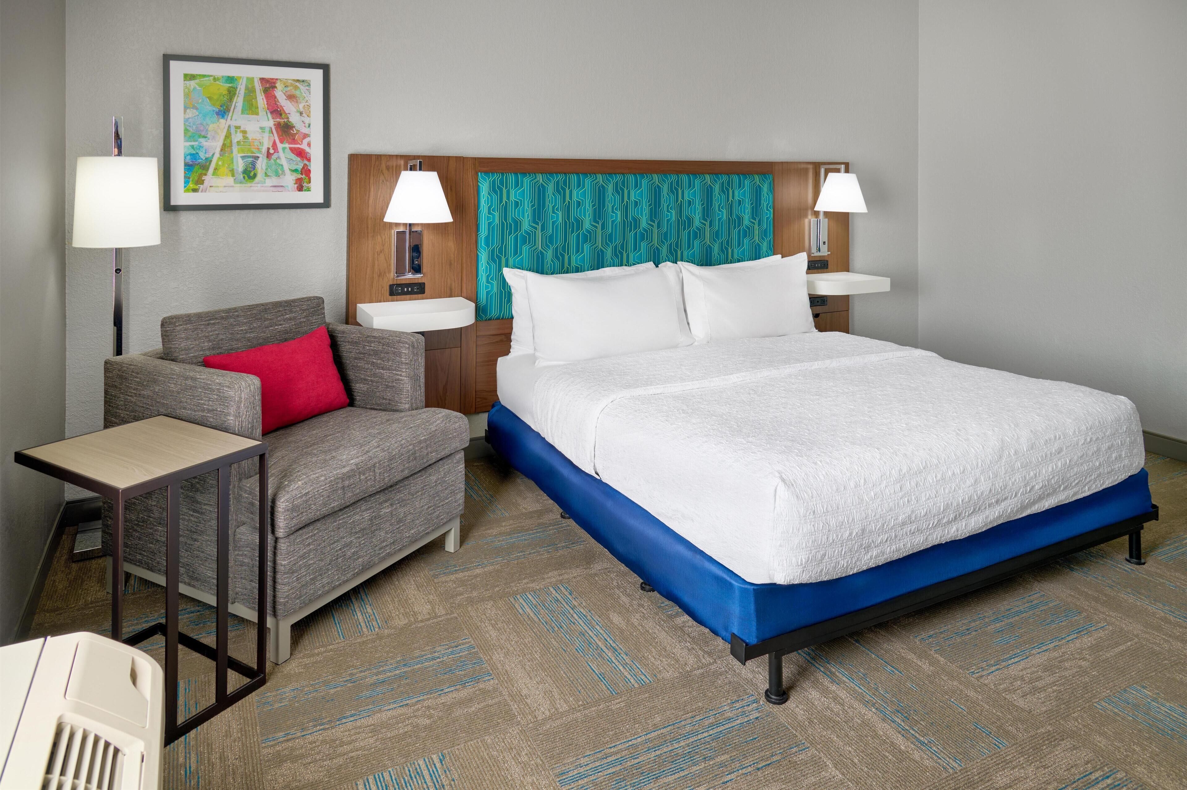 Una habitación de hotel con una cama, un sofá, dos mesitas de noche y una lámpara de pared.