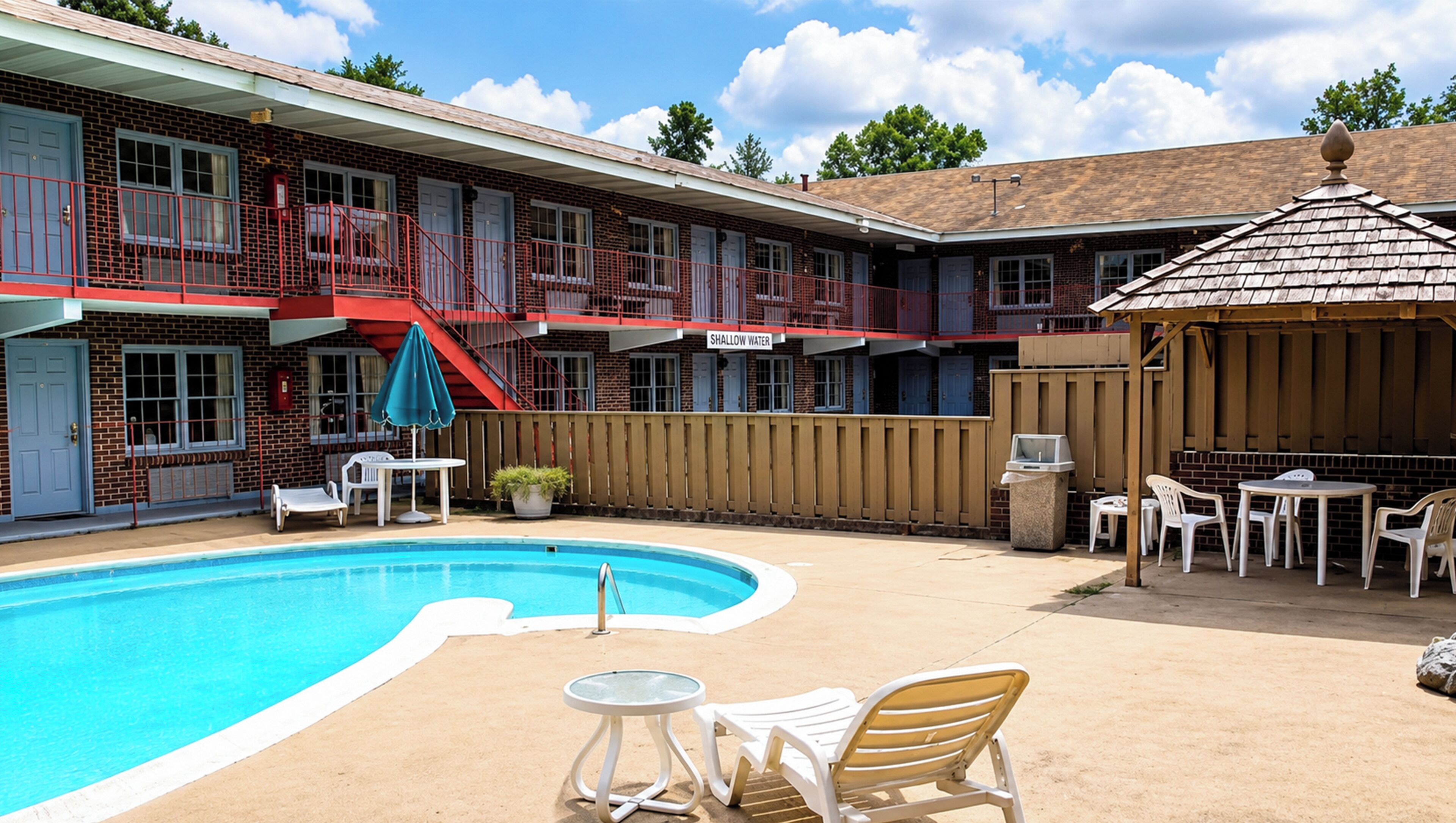 A pool area with a red railing, lounge chairs, and a sign reading 'Shallow Water'.