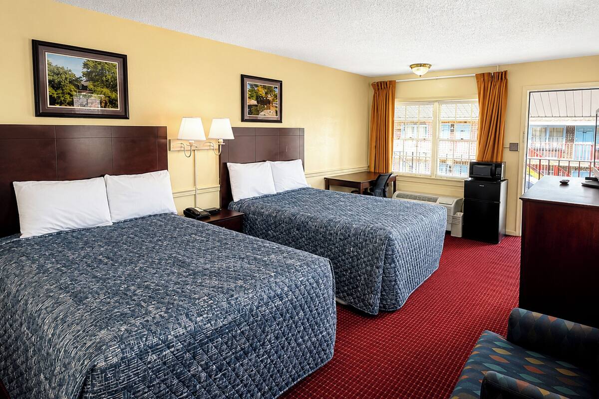 A hotel room with two beds, a desk, a television, and a window with curtains.