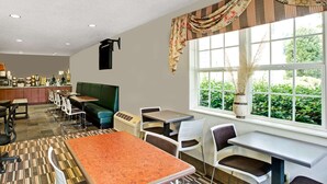 A dining area with a mix of booths and tables, a patterned carpet, and a window with a view of greenery.