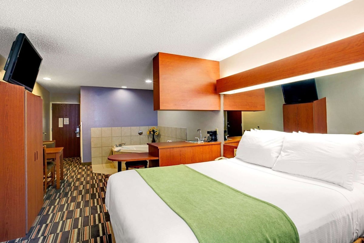 A hotel room with a bed, a desk, a sink, and a television.