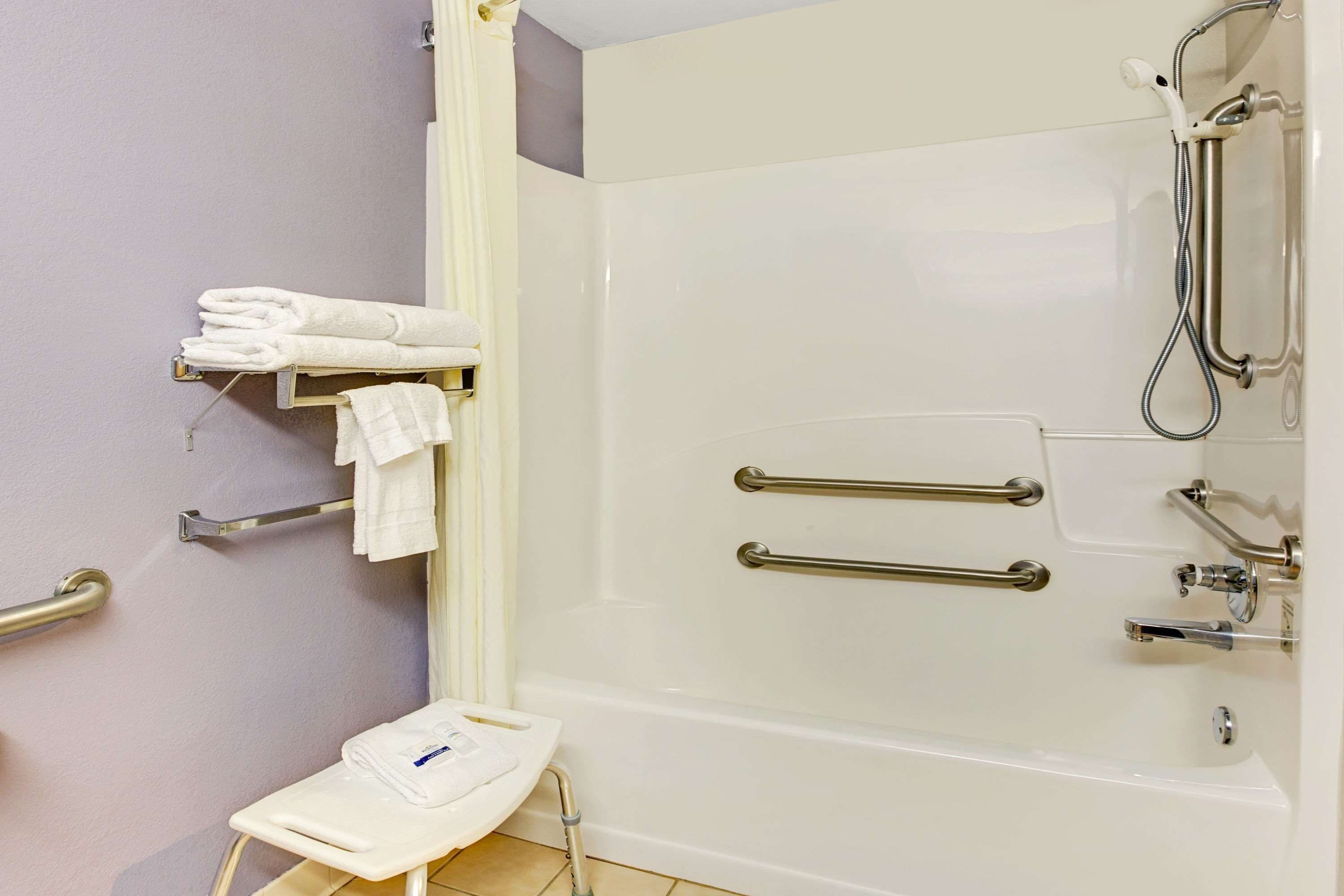 A bathroom with a walk-in shower, grab bars, a toilet with a raised seat, and a towel rack.