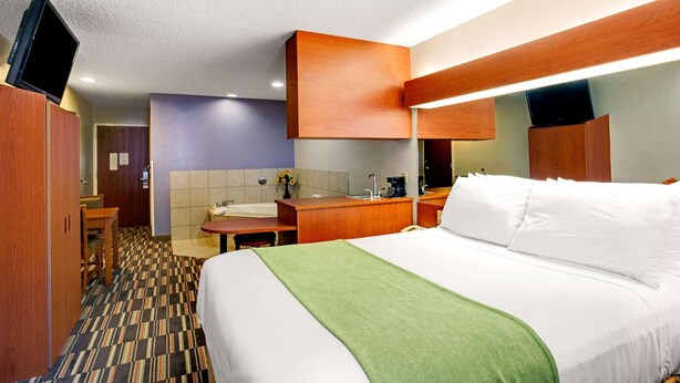 A hotel room with a bed, a desk, a chair, a bathroom with a sink and mirror, and a television mounted on the wall.