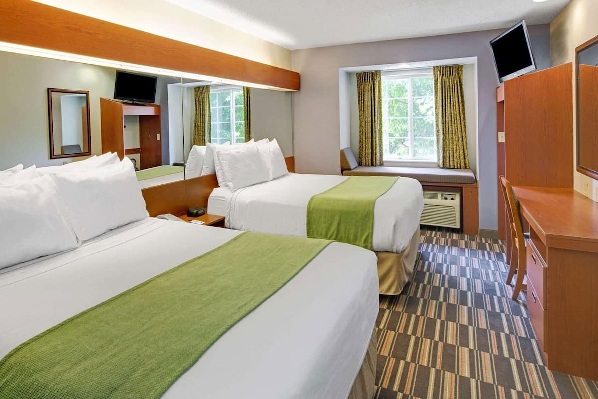 A hotel room with two beds, a desk, a television, and a window with curtains.