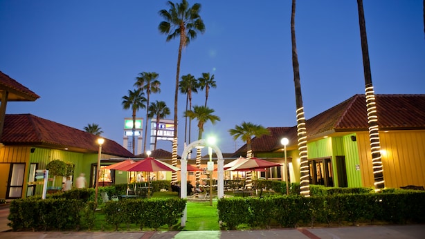 A hotel courtyard with palm trees, outdoor seating, and a green building facade. - Hotel Saddleback Los Angeles - Norwalk (Norwalk)
