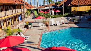 A pool area with lounge chairs and umbrellas, a pool, and a building with balconies. - Hotel Saddleback Los Angeles - Norwalk (Norwalk)