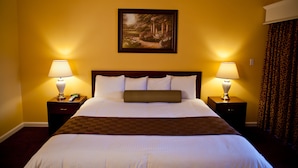 A hotel room with a large bed, two bedside tables with lamps, a painting on the wall, and a checkered throw blanket. - Hotel Saddleback Los Angeles - Norwalk (Norwalk)