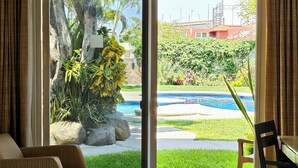 Habitación de hotel con cama, una silla y vistas a una piscina y jardín.