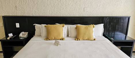 A hotel room with a large bed, two bedside tables, a telephone, and a sign on the table.