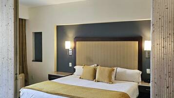Quarto de hotel com uma cama grande, um ventilador de teto, uma mesa de cabeceira e uma luminária na parede.