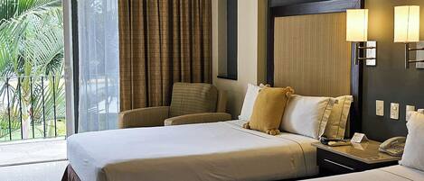 Habitación de hotel con cama, una silla, mesita de noche con teléfono y vista a palmeras a través de la ventana.