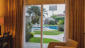Una habitación con puerta de vidrio corredera que da a una zona de piscina, una mesa de comedor con sillas y una silla de mimbre.