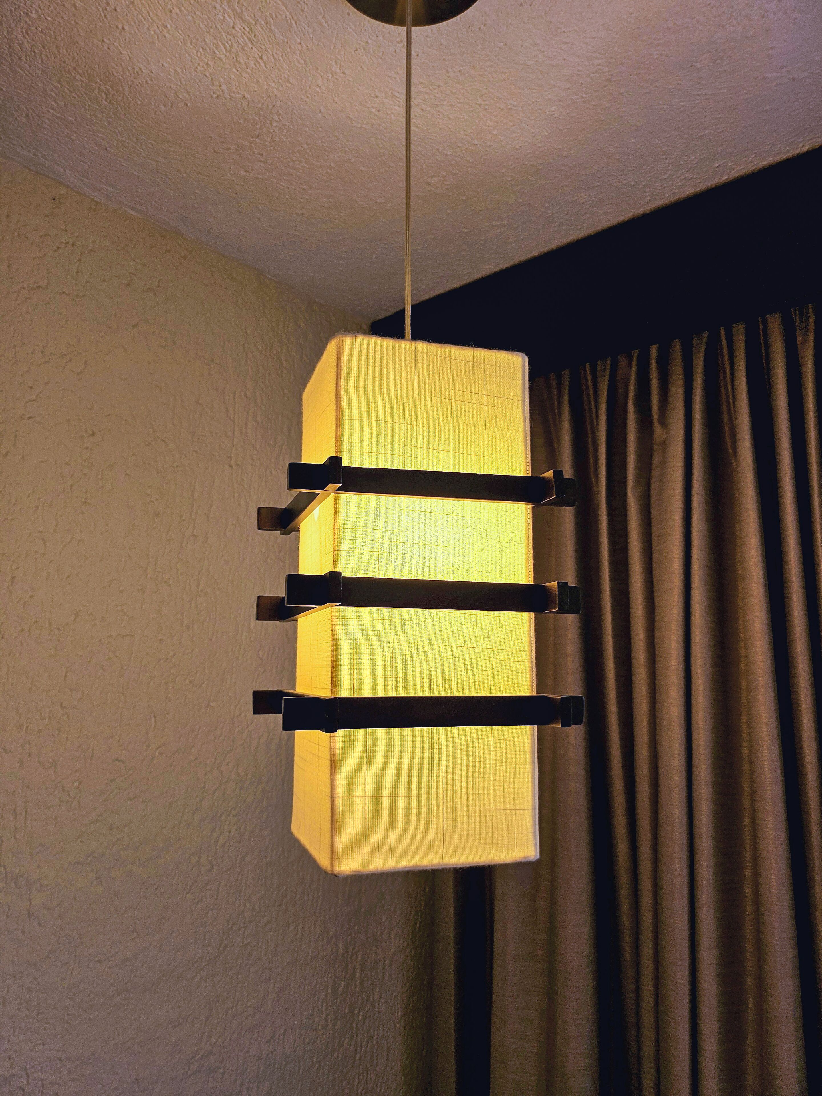 Una lámpara colgante con pantalla rectangular y tres barras horizontales.